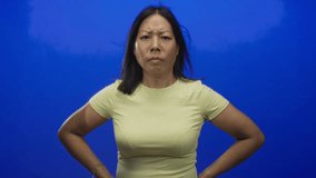 Young hispanic woman clenches fist and glares against vivid blue studio backdrop while standing firm; anger defiance resolve. - Powered by Shutterstock - Get 15% off with code: PIKWIZARD15