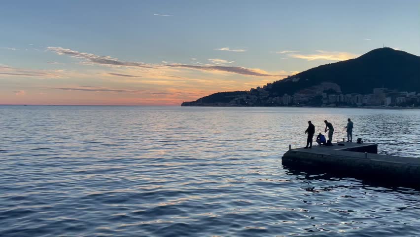 A serene and tranquil sunset view featuring people fishing from the pier, showcasing a beautiful landscape