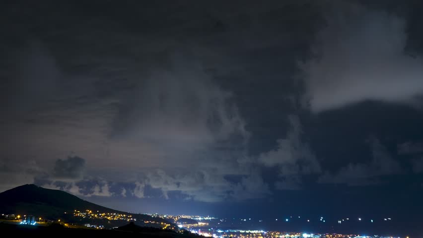 Time-lapse footage of storm clouds and lightning moving above city lights at night. A dramatic aerial view capturing the power and beauty of the sky over the Black Sea coast.