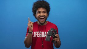 African american lifeguard man holding binoculars shows a gesture of having an idea against a vibrant blue background, embodying alertness and safety. - Powered by Shutterstock - Get 15% off with code: PIKWIZARD15