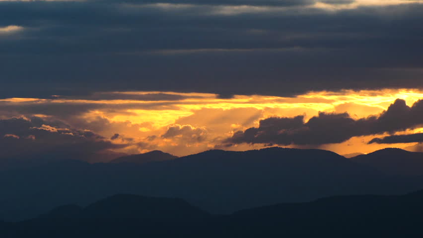 Clouds and setting sun creating God Beams over western North Carolina foothills in early Autumn, timelapse.