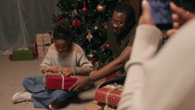 Close up on phone screen in hands of Black woman recording video of little happy daughter unpacking Christmas gift while sitting with father on floor next to present boxes in living room - Powered by Shutterstock - Get 15% off with code: PIKWIZARD15