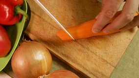 Male hands slice fresh carrot with knife on cutting board surrounded by bell pepper onion and tomatoes. Carrot slices show precision and texture. Concept of knife skills and vegetable preparation - Powered by Shutterstock - Get 15% off with code: PIKWIZARD15