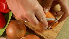 Male hands peel fresh carrot with vegetable peeler on wooden cutting board surrounded by onions, bell peppers. Peeled carrot show texture and freshness. Essential kitchen routine and healthy food prep - Powered by Shutterstock - Get 15% off with code: PIKWIZARD15
