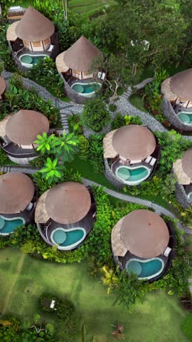 Vertical drone video showing luxury glamping tents in Bali with private pools nestled in lush tropical garden and winding stone paths, capturing peaceful eco luxury and modern island design aesthetics