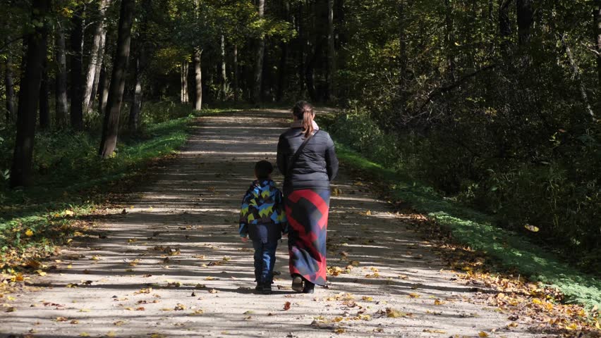 A Mother and Son Walking Away as Autumn Leaves Fall Around Them