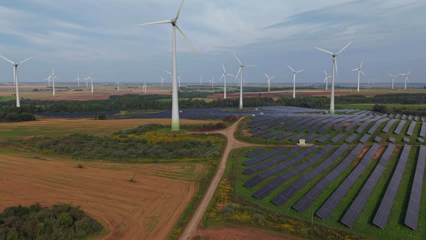 Drone view of a renewable energy farm featuring wind turbines and solar panels across expansive rural farmland, symbolizing clean energy innovation and sustainability.