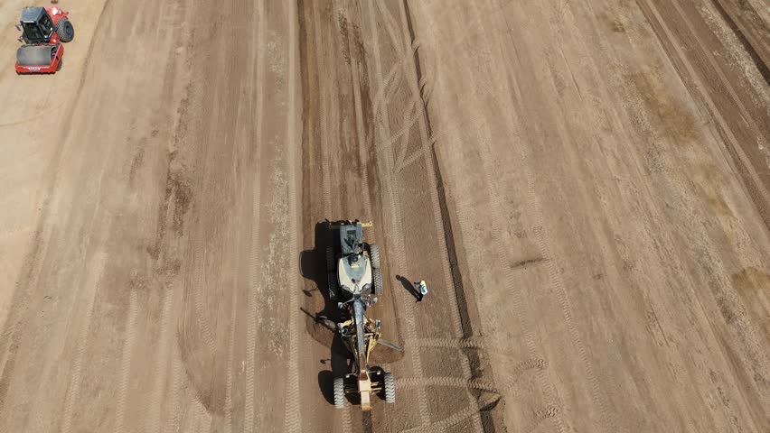 Drone aerial footage showing a motor grader leveling soil at construction site. ground textures and engineering precision during earthwork - civil engineering, road construction, heavy equipment