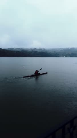 Kayakers paddling on a lake under clouds and heavy rain. Sport in bad weather conditions. Late autumn kayaking. 