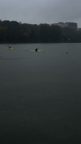 Kayakers paddling on a lake under clouds and heavy rain. Sport in bad weather conditions. Late autumn kayaking. 