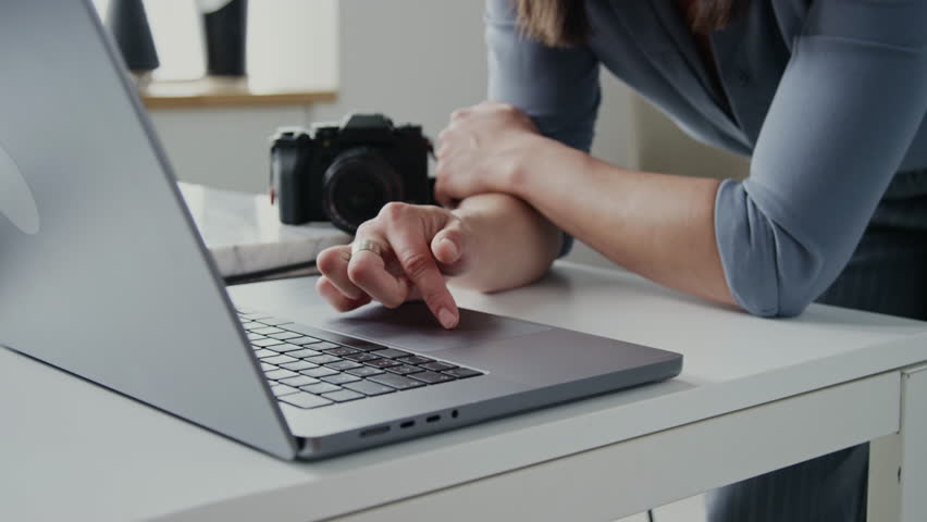 Close up of young brunette professional photographer sorting new photos on laptop and adjusting her glasses