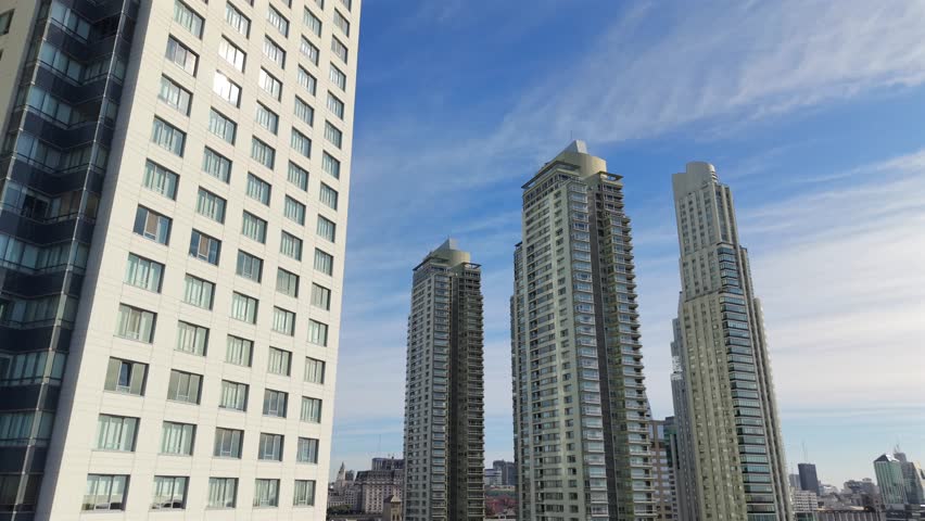 Reveal shot over Puerto Madero, unveiling Buenos Aires’ skyline—Alvear Tower, El Faro Towers, and YPF Tower gleam against wispy clouds, reflecting Argentina’s modern pulse and architectural ambition