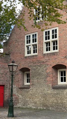 Vertical video of the building exterior of an old Dutch house made of red bricks outdoor at daytime framed by autumn leaves during fall season in Leiden in The Netherlands.