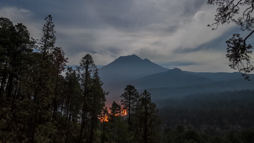 Timelapse of an active forest fire at Volcán Popocatépetl during the night, illuminated by a full moon and dramatic skies.