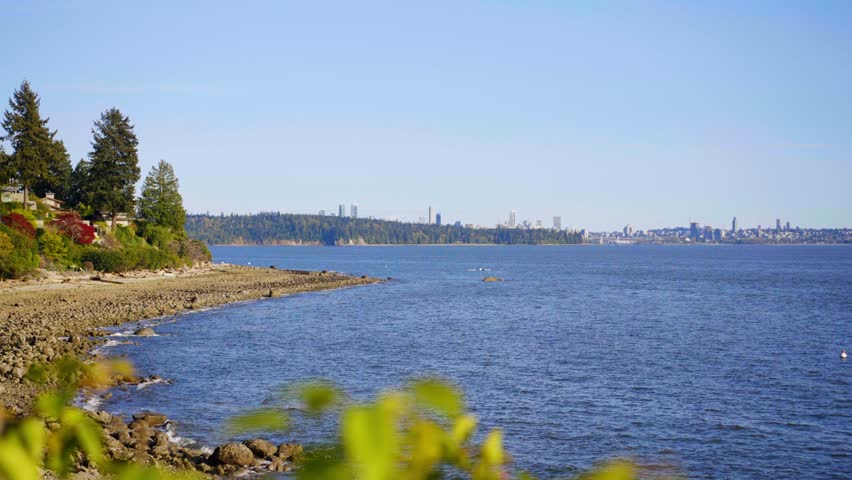 A scenic shot of the beach and the blue waters of the sea in West Vancouver, Canada with Vancouver City over on the horizon.