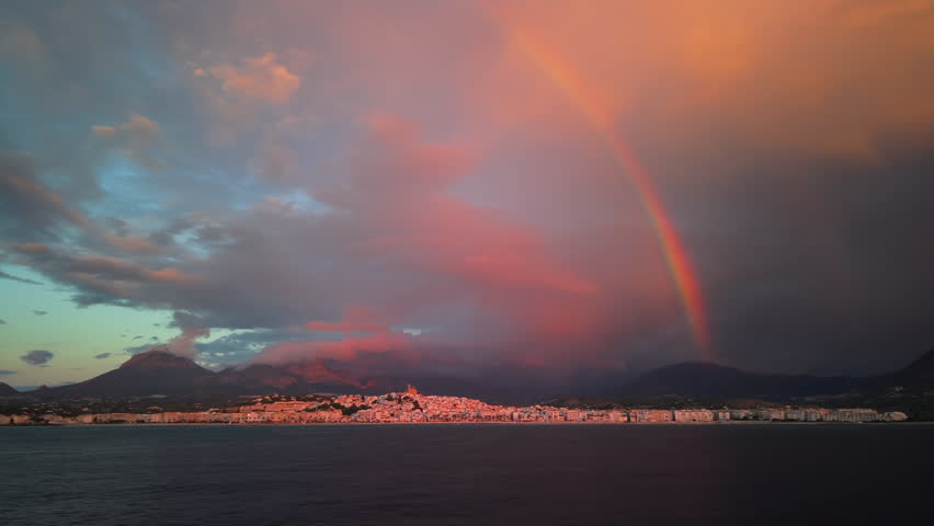 Rainbow over the coastal city of Altea, Spain, during a dramatic sunset with colorful clouds and mountains in the background. High quality 4k footage