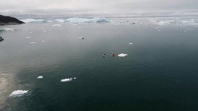 Aerial drone footage of kayakers paddling through icy Arctic waters surrounded by floating icebergs in Greenland, capturing the remote wilderness, cold beauty, and adventure of polar exploration. - Powered by Shutterstock - Get 15% off with code: PIKWIZARD15