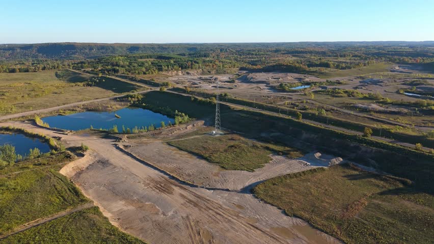 Drone shot flying forward toward a telecommunication tower surrounded by gravel pits, ponds, and open terrain in Caledon, Ontario, Canada
