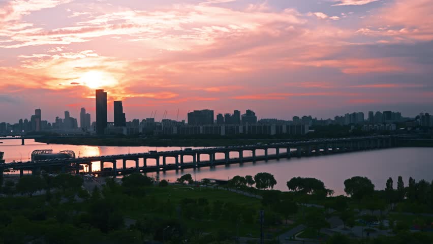 Expansive aerial shot captures Banpo Bridge traffic silhouetted against Seoul city skyline with vivid sunset colors reflecting on the Han River