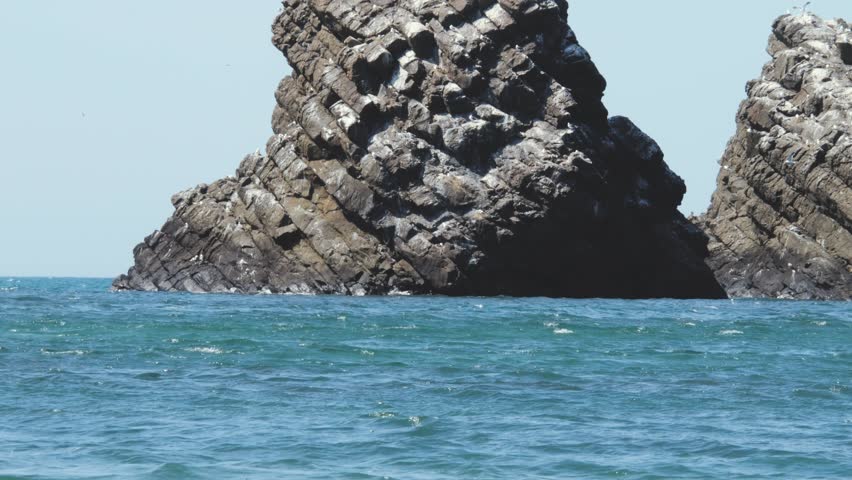 Huge Majestic Rocks in the Sea Slow Mo. An amazing natural phenomenon. Mighty mountains washed by the sea. Seagulls, summer, and wildlife.