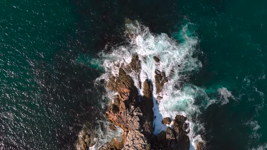 Topdown View Of Foamy Waves Breaking Onto Rocky Coastline. Aerial Slow Motion Shot