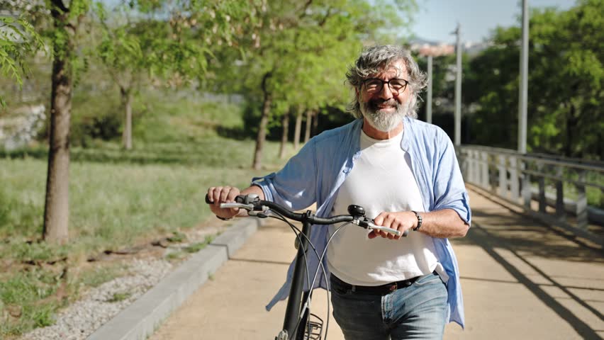 Old Man walking pushing Bicycle in Public Park. Healthy and active relaxing lifestyle for seniors 