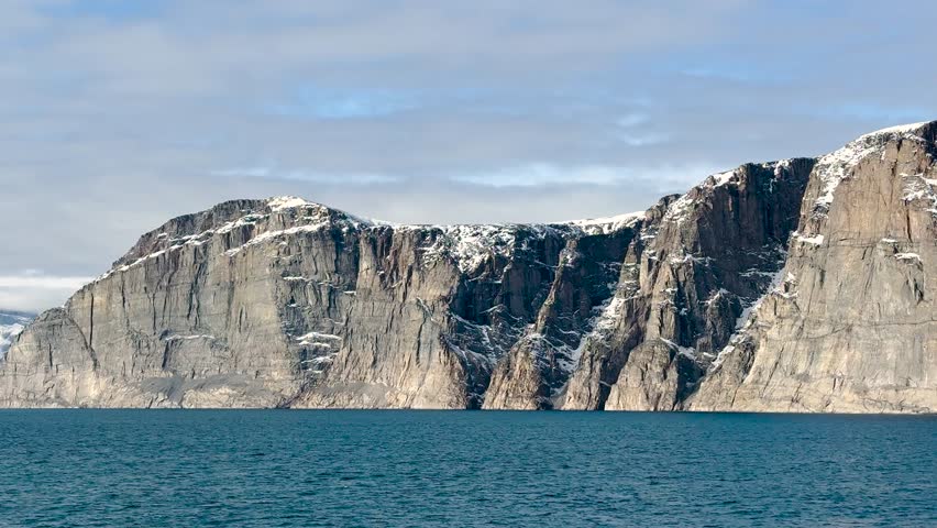 Witness the magnificence of Baffin Island’s coastal landscapes. The video captures impressive cliffs rising above calm blue waters, highlighting nature
