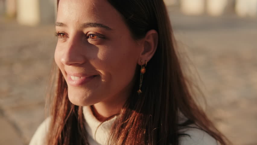 Young woman smiles in Seville, Spain at golden hour. She shields her eyes from the sun. Joyful travel and tourism concept.