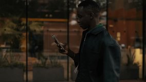 A young man checks his phone while walking past a cafe at night. He smiles, likely at something he's seen. Perfect for projects about social media, city life and communicating. - Powered by Shutterstock - Get 15% off with code: PIKWIZARD15