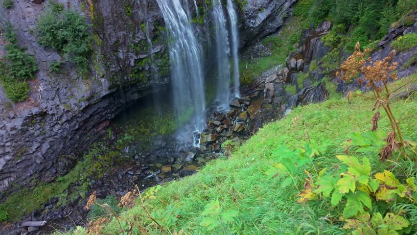 A scenic view of the beautiful Narada Falls cascading through a vibrant green forest at Mount Rainier National Park