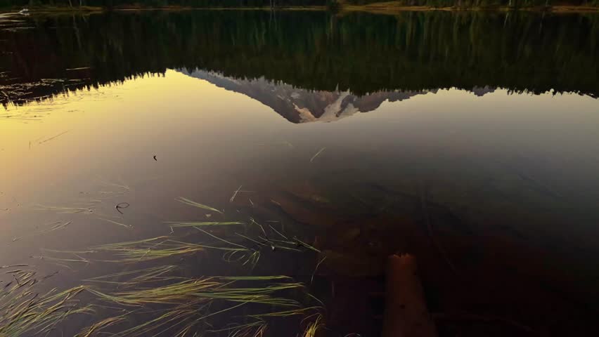 A stunning golden sunset paints the sky over Mount Rainier, with its majestic reflection perfectly captured in the still waters of Mirror Lake
