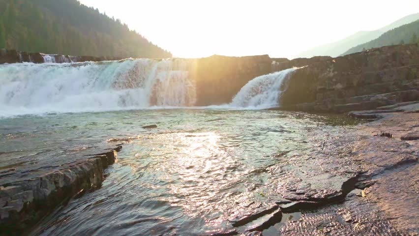 A magnificent and breathtaking view of Kootenai Falls, bathed in the warm, golden light of sunrise, highlighting its powerful cascades and natural beauty
