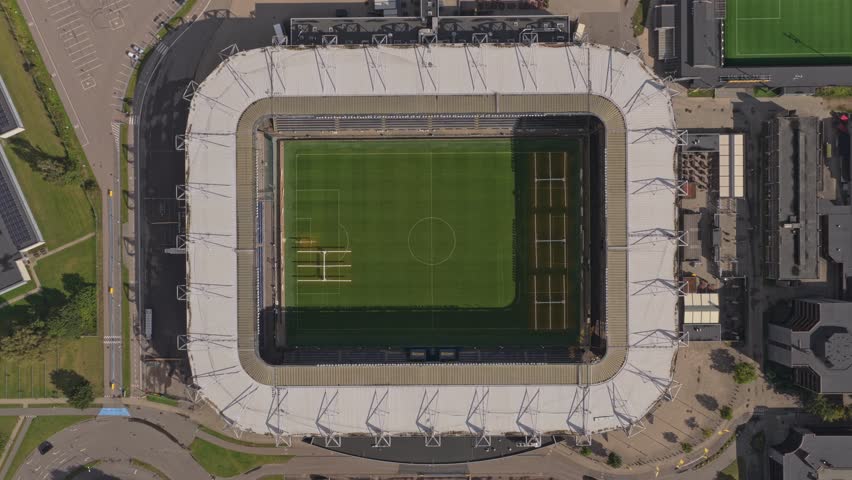 Top-down view of Brondby IF stadium—geometric seating bowl, technical areas, and crisp touchlines under a modern roof.