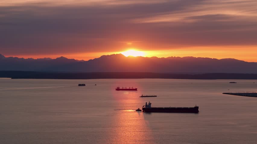 Sun setting over the Olympic Mountains with large freight ships passing through the Puget Sound.