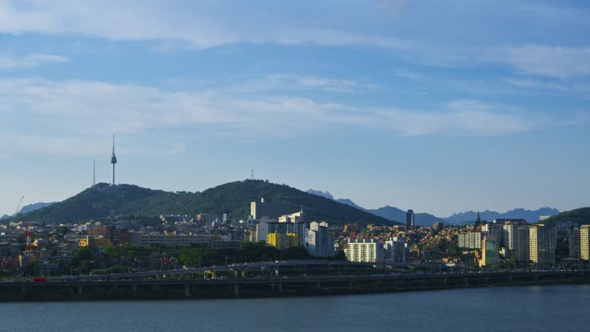 Wide city view of Seoul featuring Namsan Tower and Han River from above, showing traffic and Yongsan skyscrapers under clear summer sky