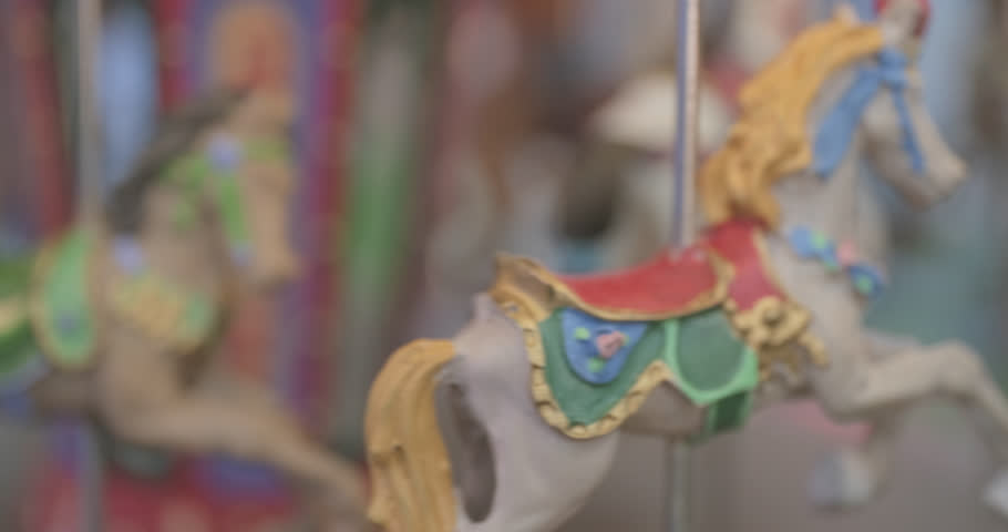Generic retro style toy carousel is spinning, horse figures are moving. Close up handheld shot, artificial lighting, real time speed.