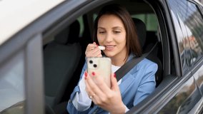 Attractive woman with a pleasant smile sits in her car while applying makeup. Using the camera on her smartphone as a reflection, she carefully applies lip balm before heading to work - Powered by Shutterstock - Get 15% off with code: PIKWIZARD15