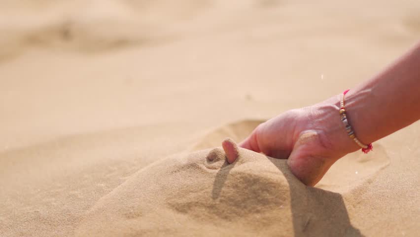 Close up shot of hand dropping golden sand in the air In Dubai desert during bright sunny day in Dubai, UAE. Tourist girl enjoying and exploring sand dunes of Dubai. Travel and holidays concept