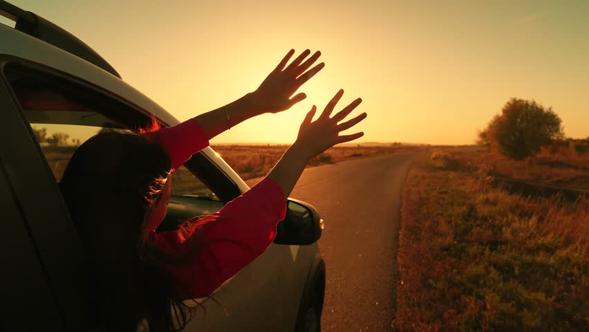 Young female passenger catches wind with hands from car window. Beautiful girl student in car drives road to meet sunrise. Family trip, teenage girl traveling by auto. Family vacation. People travel