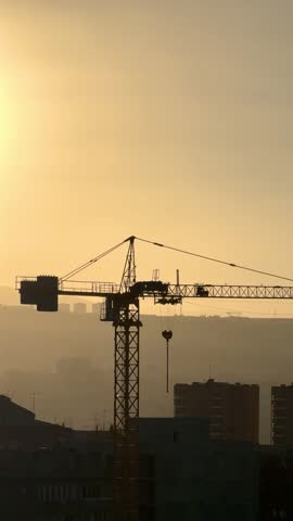 Construction crane against the backdrop of a city with a bright sun . A crane is in the sky above a city at day The crane is tall and is in the middle of the sky
