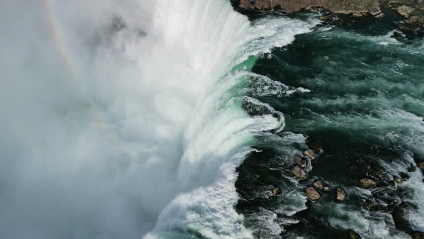 Drone footage capturing a beautiful rainbow forming in the mist as water crashes down the falls — pure natural magic