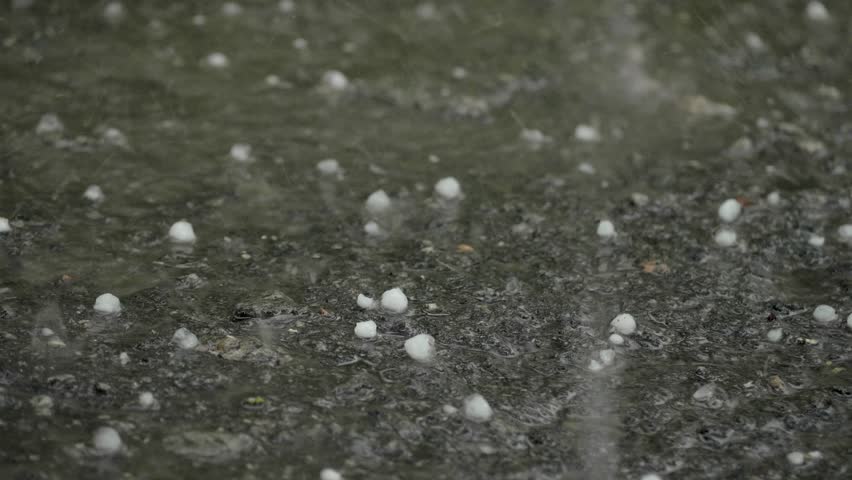 The ground is bombarded by hail and rain, with the icy pellets bouncing off the soil and the rainwater forming puddles, saturating the earth and creating muddy patches across the landscape