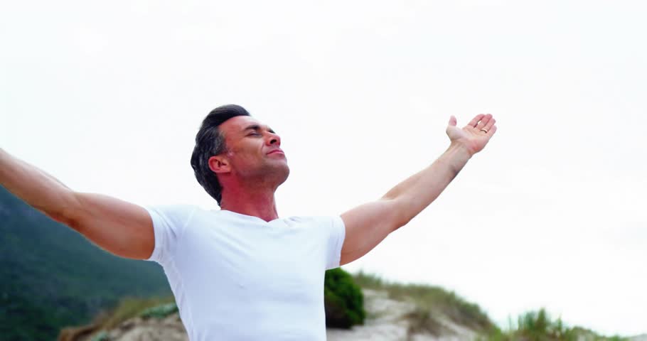 Mature adult man lifting arms on sandy hillside activating golden orange particles swirling torso. Resilience, vitality, spirituality, warmth, landscape, serenity, energy