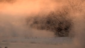 Dense mist rises from a tranquil river, shrouding frost covered trees and snow laden banks in a serene winter landscape under a warm sunrise sky - Powered by Shutterstock - Get 15% off with code: PIKWIZARD15