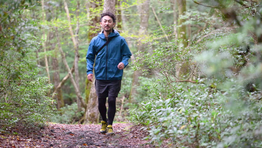 A middle-aged Japanese man running on a forest road deep in the woods. Full body.