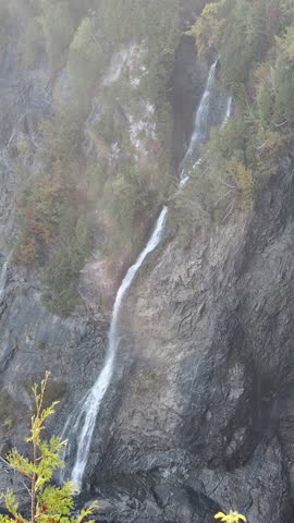 Small mountain waterfall flowing down rocky cliff surrounded by autumn forest near Montmorency Falls