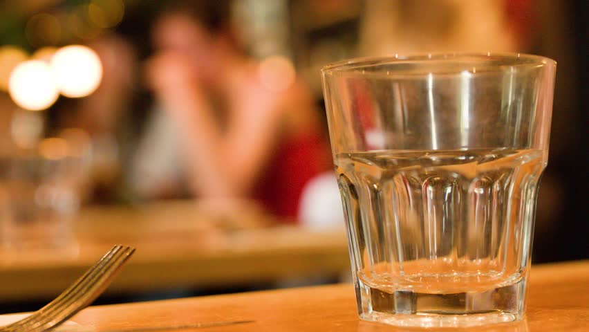 Close-up of water being poured into glass, warm ambient lighting, shallow depth of field