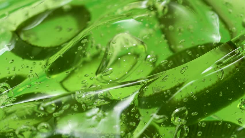 Serum gel texture with aloe vera leaf slices, green transparent cream background