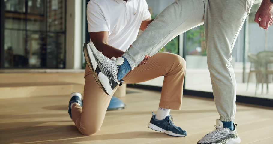 Fitness, personal trainer and stretching legs in home for health, physiotherapy support or flexibility training. Man, people or coach helping with balance exercise for mobility, movement and wellness