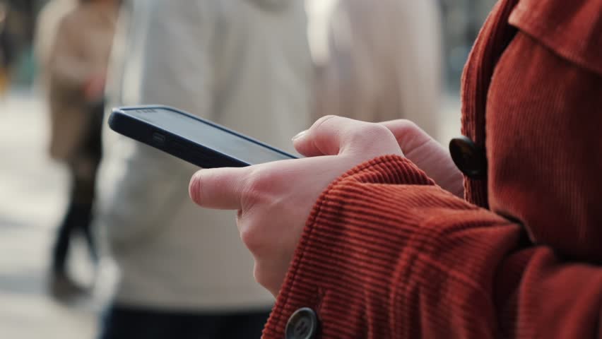 Woman walking and using a smartphone on the street in a European city. Tourist enjoying a stroll, texting on her mobile phone outdoors. High quality 4k footage